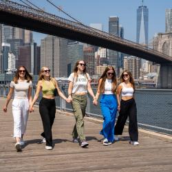 fünf au pairs laufen nebeneinander vor der Brooklyn Bridge